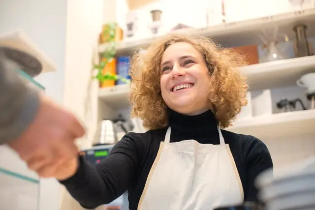 Una barista sonríe al dar la mano a un cliente en su cafetería